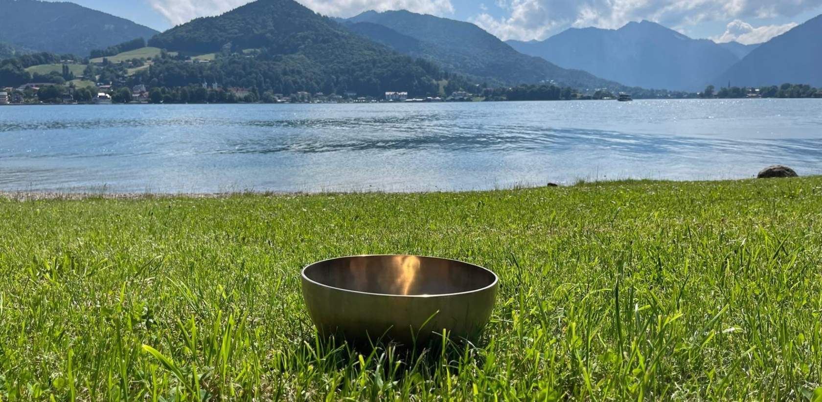 Klangschale im Gras vor einem See mit Bergkulisse im Hintergrund